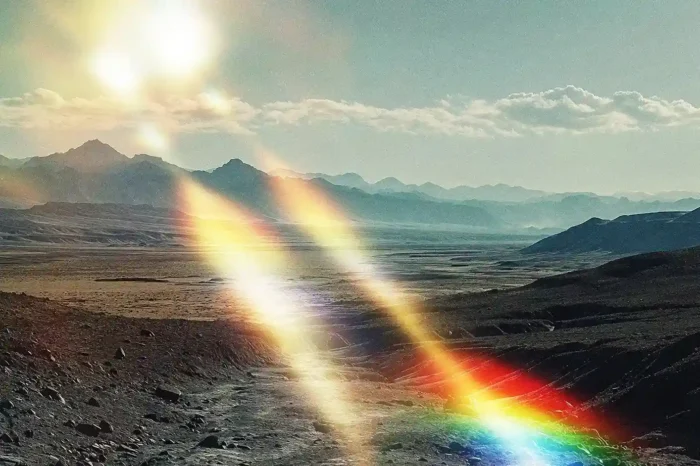 Solar flare texture overlay creating dreamy rainbow light leaks over a desert mountain landscape.