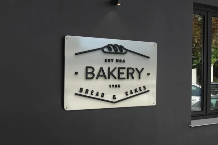Metal storefront sign mockup for bakery branding, featuring 3D text and mounted on a dark wall with realistic lighting.